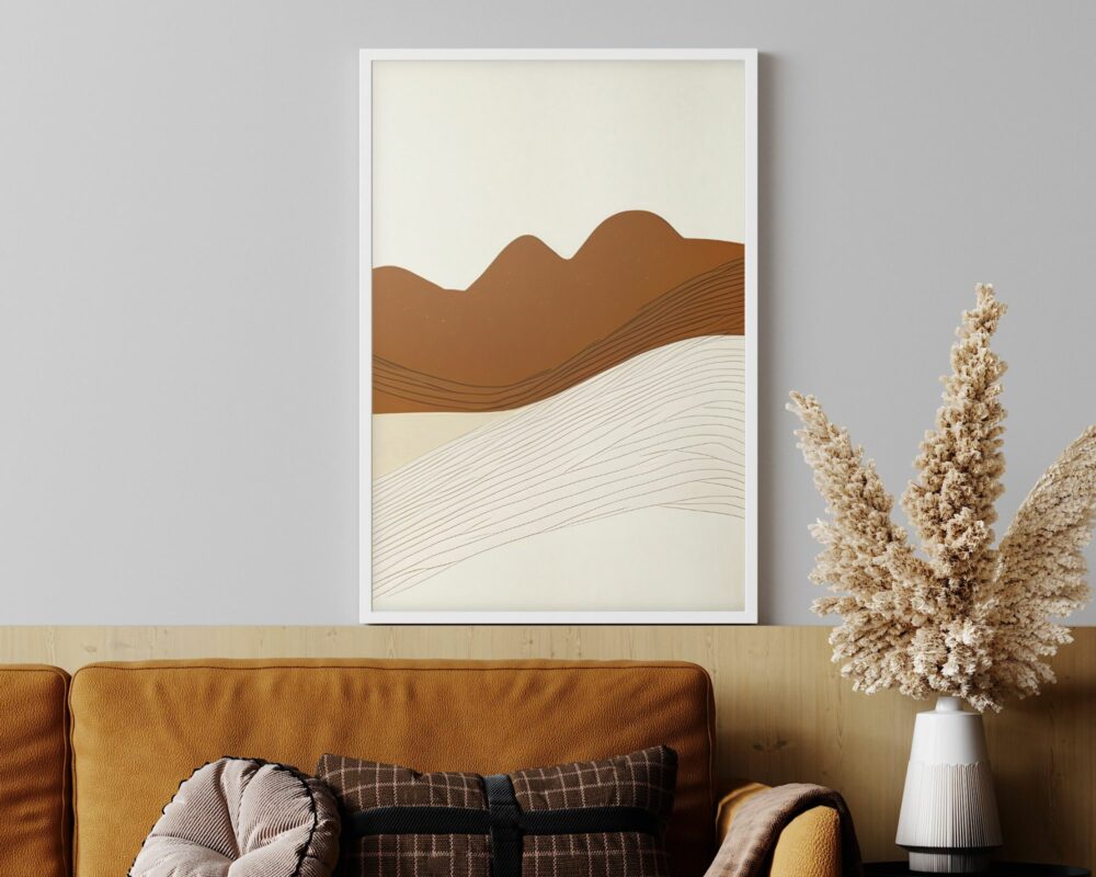 סלון מינימליסטי כולל ספה חומה עם כרית נוי. יצירת אמנות אבסטרקטית ממוסגרת בשם "תמונה לחדר שינה נוסח בוהו שיק של הרים מדבריים בצבעי בז' וחום" תלויה על קיר אפור, ומציגה גוונים בז' וחום המתארים הרים וקווים זורמים. אגרטל עם דשא פמפס בצבע בז' רך יושב על שולחן עץ מימין.