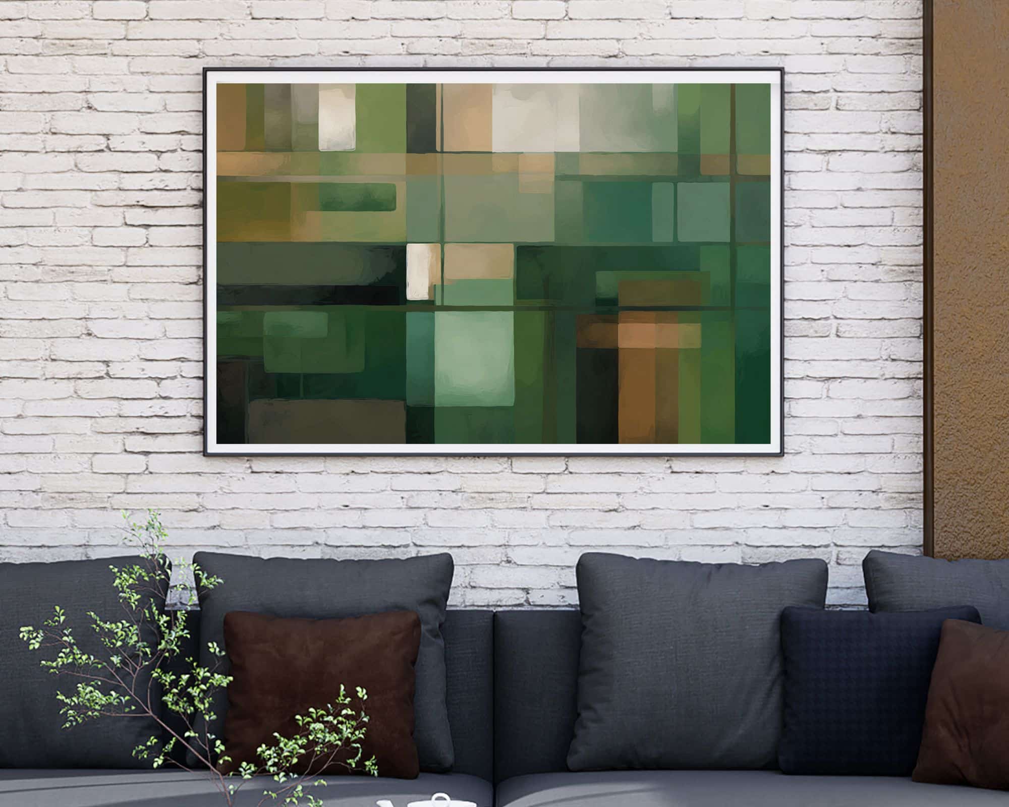 9255mo1 ציור מופשט ממוסגר הכולל צורות גיאומטריות ירוקות תלוי על קיר לבנים לבנים. מתחת, ספה אפורה כהה עם כריות חומות ואפורות יושבת על הקיר. צמח קטן עם ענפים עדינים מוצב מול הספה.