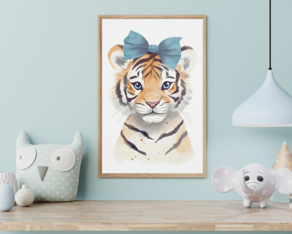 תמונה ממוסגרת שכותרתה "טיגריס בייבי עם פפיון תכלת בצבעי מים" מוצגת על קיר תכלת. התמונה ממוקמת בין ינשוף קטיפה לפיל קטיפה על שולחן עץ. מנורת תליון לבנה תלויה בצד ימין מעל השולחן.