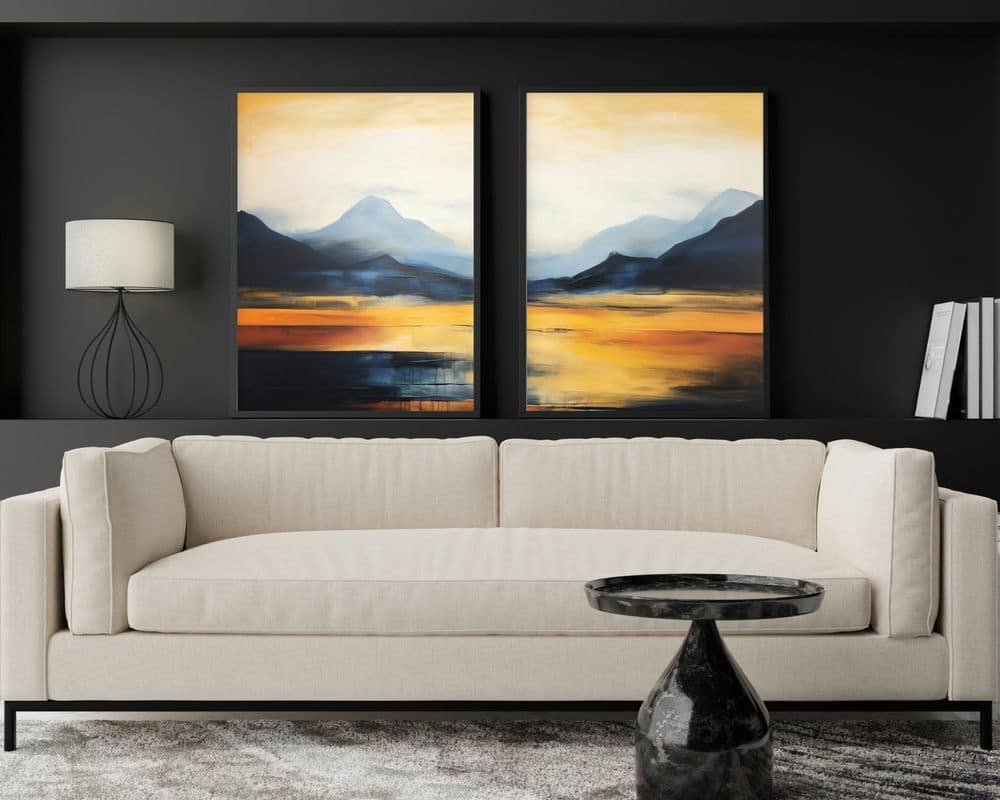 סלון מודרני עם ספה ניטרלית על קיר כהה. מעל הספה שני ציורי נוף מופשטים מתוך הסט "סט 2 תמונות לסלון אבסטרקט הרים בכחול וכתום", הכוללים הרים ושקיעה חמימה וזהובה. שולחן קפה משיש שחור ומנורה חלקה משפרים את העיצוב העכשווי.