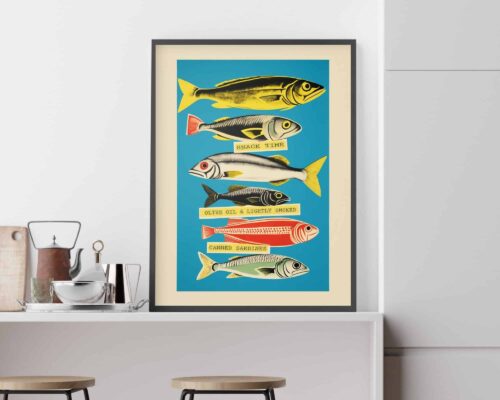 פוסטר ממוסגר מעל דלפק במטבח מתאר דגים צבעוניים שונים המסומנים במילים כמו "זמן חטיף", "שמן זית ועישון קל" ו"סרדינים משומרים". זה חלק מהתמונה למטבח ולפינת אוכל נוסח קולאז' רטרו סרדינים צבעוניים על רקע תכלת דגם א'. מתחת, יש פריטי מטבח כמו קומקום, צנצנת וכלים על השיש, עם שני שרפרפי עץ.