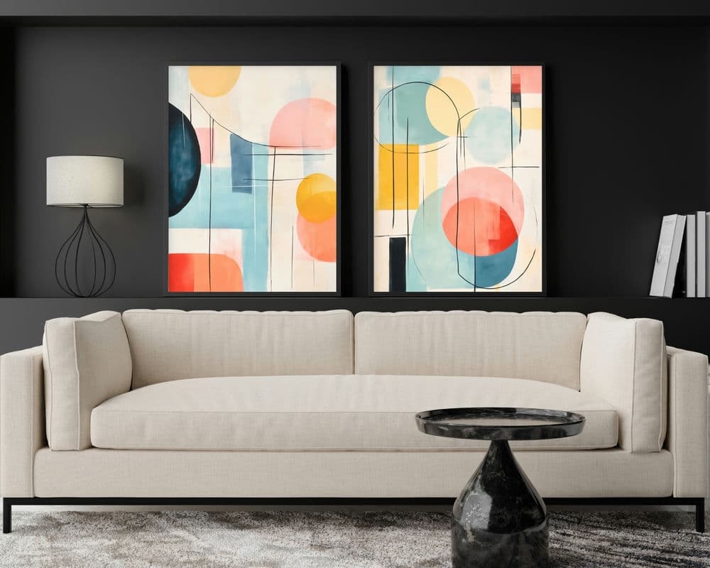 סלון מודרני עם ספה בז', שולחן קפה משיש שחור, וסט 2 תמונות לסלון נוסח אבסטרקט עיגולים צבעוניים על הקיר האפור כהה. יצירת האמנות המופשטת כוללת צורות גיאומטריות באדום, כחול, צהוב וורוד. מנורת שולחן דקורטיבית וכמה ספרים מונחים על מדף מעל הספה.