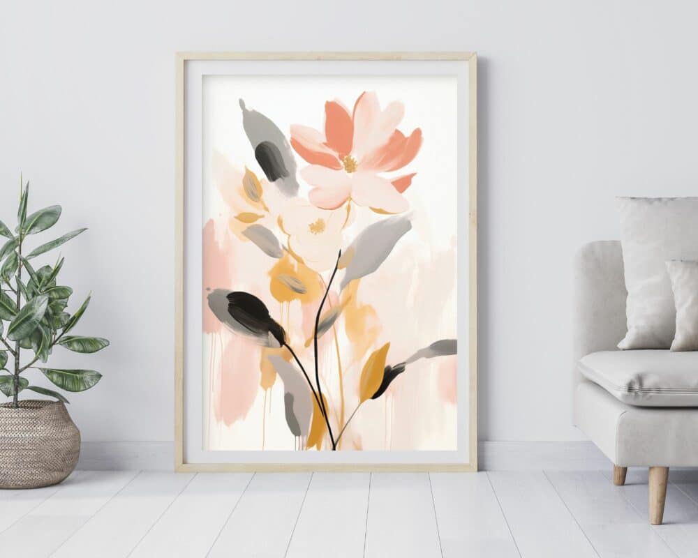 יצירת אמנות ממוסגרת בשם "תמונה לחדר שינה נוסח מופשט פרח בצבע ורוד ונגיעות זהב" המתארת פרח ורוד גדול עם פריחה קטנה יותר, מוקף בעלים בגוונים משתנים של ירוק, צהוב ואפור. המסגרת מונחת על הרצפה על רקע קיר אפור בהיר, לצד צמח בסל ארוג וחלק מספה בז'.