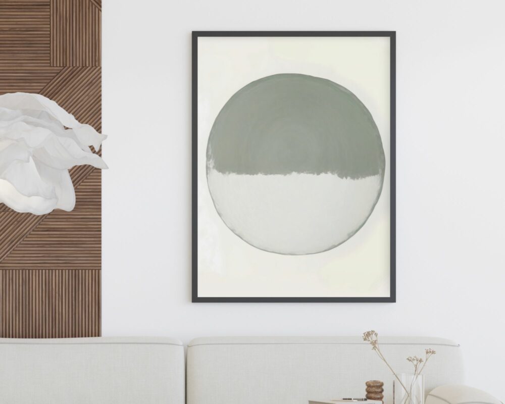 ציור מינימליסטי שכותרתו "תמונה לחדר שינה נוסח מינימליסטי עיגול לבן וירוק מרווה" במסגרת שחורה תלוי על קיר לבן. הגרפיקה כוללת עיגול גדול וממורכז כאשר החצי העליון בצבע אפור והחצי התחתון בלבן. מתחת לציור ספה לבנה עם שולחן צד מעץ ובו פרחים מיובשים. משמאל, יש קטע של חיפויי עץ עם מרקם ויצירת נייר לבן ומקומט.