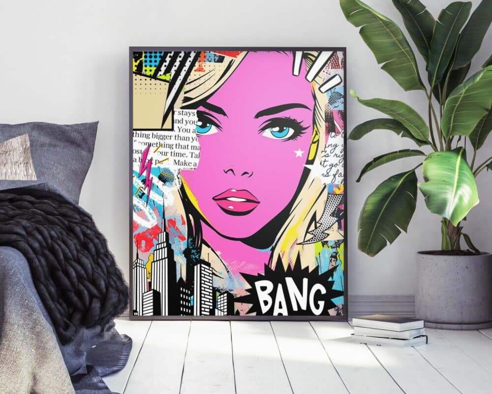הדפס ממוסגר פופ ארט תוסס בשם "תמונה לחדר נוער נוסח פופ ארט אישה ורודה בעיצוב קומיקס דגם א'" מציג אישה בלונדינית עם עור ורוד ועיניים כחולות, מסוגננת בסגנון קומיקס עם המילה "BANG" באותיות מודגשות. הוא מוצג על הרצפה ליד מיטה נעימה, ליד עציץ, על רקע קיר לבן.