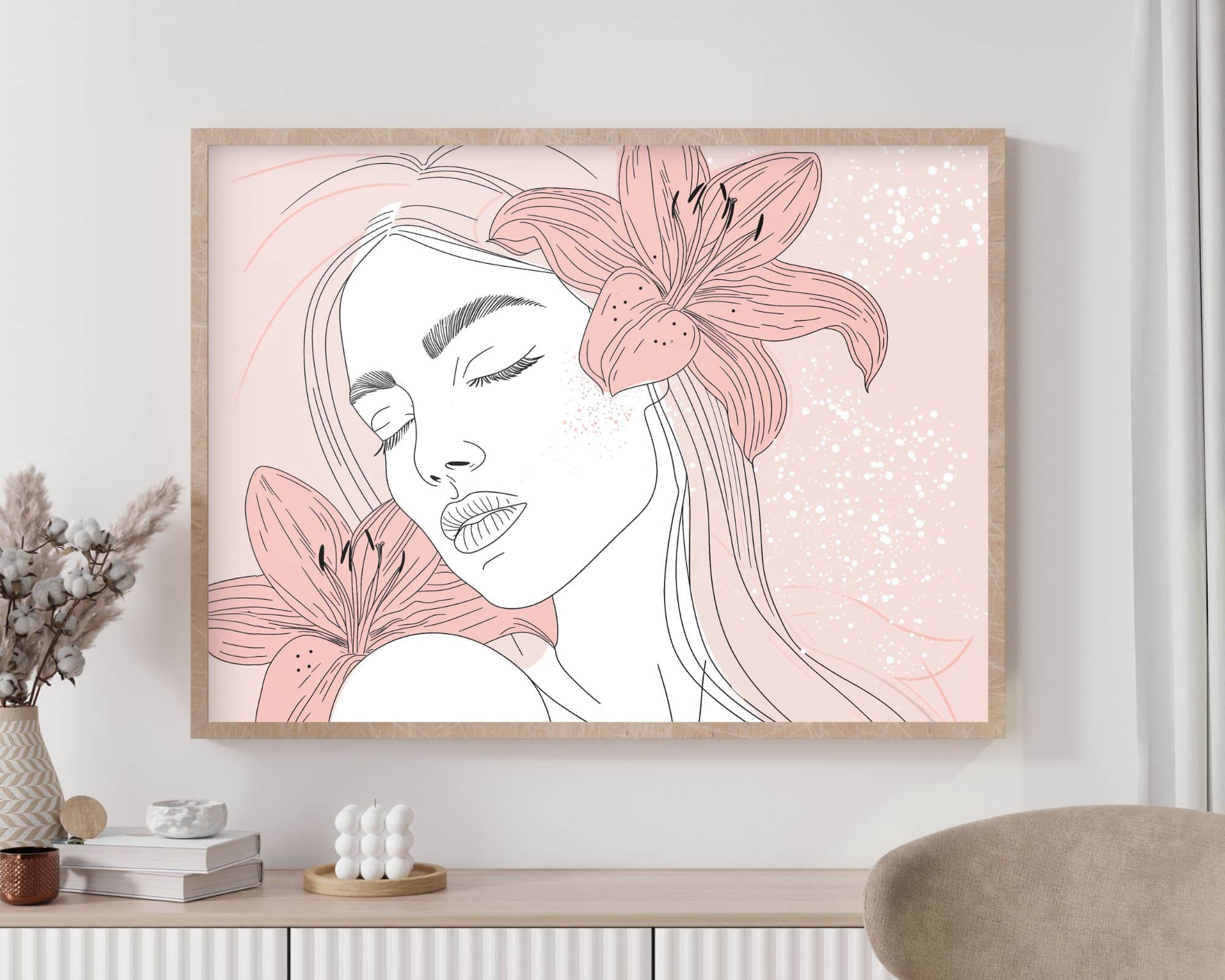 2596mo1 יצירת אמנות ממוסגרת מהקולקציה "תמונה מעל המיטה בעיצוב מינימליסטי אישה ושושנים רודים" תלויה על קיר בז', הכוללת ציור קו מסוגנן של אישה עם עיניים עצומות, שיער ארוך וחבצלות גדולות סביב ראשה. הרקע ורוד בהיר עם כתמים לבנים. למטה, מזנון עם תפאורה כולל פרחים מיובשים ופסל קטן.