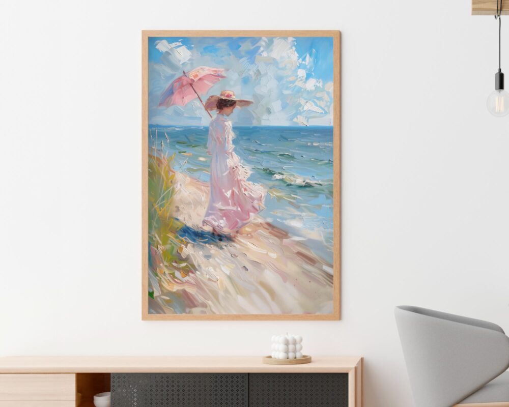 "תמונה לפינת אוכל נוסח ציור וינטג' גברת על חוף הים" ממוסגר תלויה על קיר לבן מעל ארון נמוך וליד כיסא אפור. הציור מתאר אישה בשמלה ורודה זורמת וכובע אוחזת בשמשיה ורודה, עומדת על שפת הים עם גלים ושמים מעוננים ברקע.
