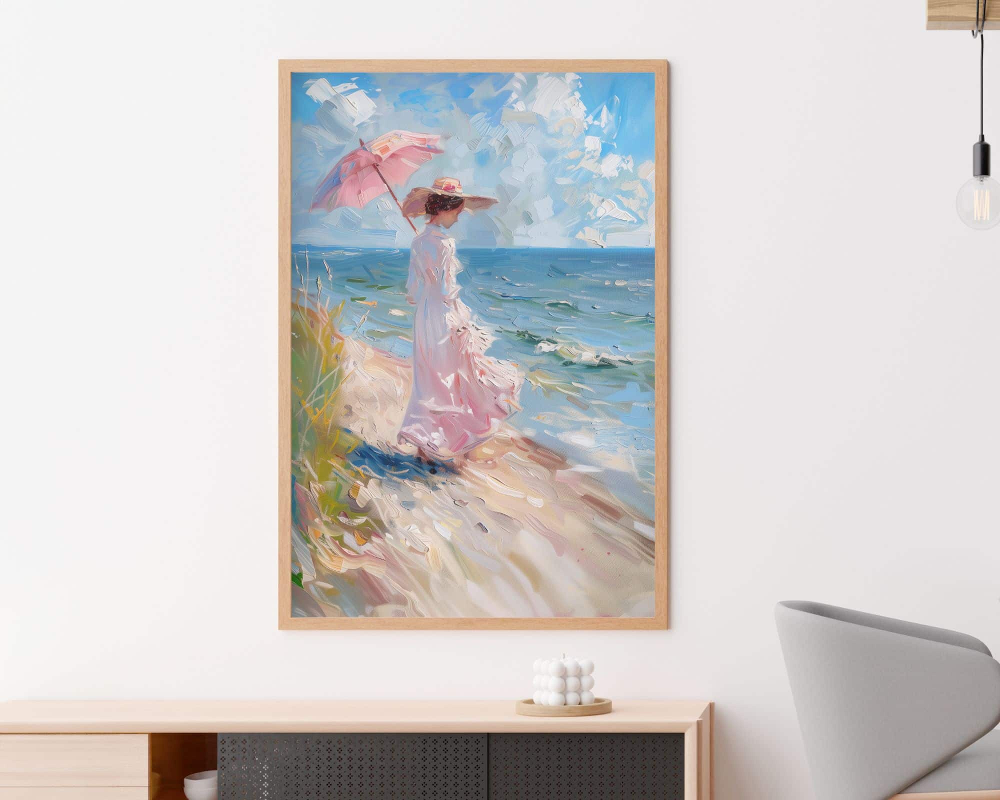 2621mo1 "תמונה לפינת אוכל נוסח ציור וינטג' גברת על חוף הים" ממוסגר תלויה על קיר לבן מעל ארון נמוך וליד כיסא אפור. הציור מתאר אישה בשמלה ורודה זורמת וכובע אוחזת בשמשיה ורודה, עומדת על שפת הים עם גלים ושמים מעוננים ברקע.