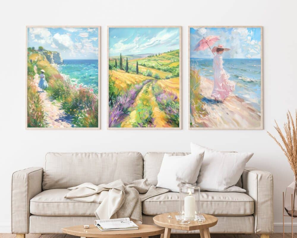 ספה בז' עם כריות לבנות ובז' יושבת מול קיר לבן המעוטר ב"סט 3 תמונות לסלון מעל הספה נוסח וינטג' אישה בים" - סט של שלושה ציורי נוף תוססים. הראשון מתאר שביל חוף, השני אזור כפרי הררי, והשלישי מציג אישה עם שמשיה ורודה ליד הים. שולחן עץ עגול עם נר וספרים נמצא בחזית הספה, בעוד עשבים מיובשים באגרטל מונחים בצד ימין.