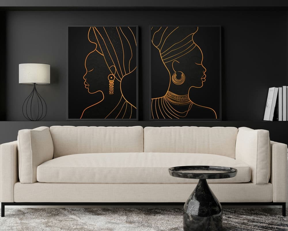 סלון מודרני כולל ספה בצבע בז' בהיר עם שולחן קפה קטן משיש שחור בחזיתה. מעל הספה נמצאת "סט 2 תמונות לסלון מינימליסטי נשים אפריקאיות", המציגה פרופילים אלגנטיים של נשים מעוטרות בעיטוף ראש ותכשיטים באומנות מינימליסטית בשחור וזהב. מנורה וספרים ממוקמים משני הצדדים.