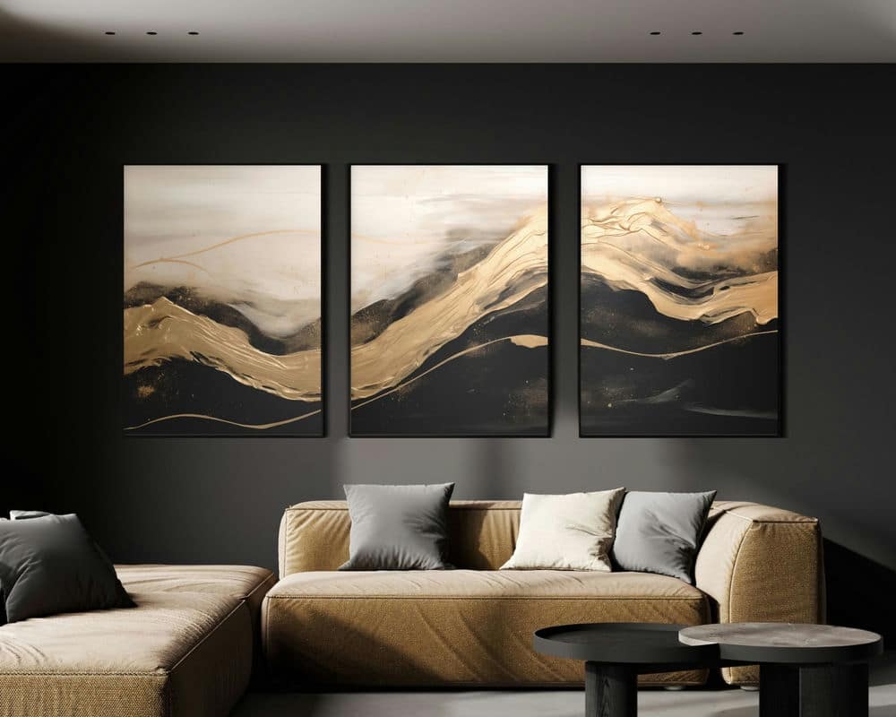 סלון מודרני כולל ספת חלוקה בז' עם כריות אפורות ובז'. מוסיפות כישרון מעל הספה הן סט 3 תמונות סלון זהב בין שחור ולבן לסגנון מינימליסטי, המציגות שלושה ציורים מופשטים בגוונים של שחור, זהב ולבן על רקע קיר כהה. מול הספה מוצבים באלגנטיות זוג שולחנות קפה עגולים ושחורים.