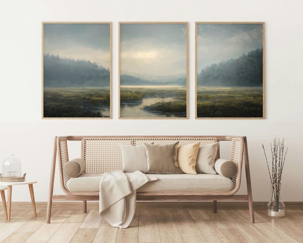 סלון מינימליסטי כולל ספסל עץ עם כריות לבנות ובז' וזריקה קלה. מעל הספסל, שלוש תמונות לסלון ממוסגרות מהסט 3 תמונות לסגנון וינטג' נחל עובר ביער מתארות אגם ערפילי מוקף גבעות מיוערות. עיצוב החדר כולל כד זכוכית וסידור צמחים מיובשים.