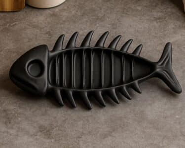 מגש עצמות דג בצבע שחור מט, בעיצוב צורת דג עם ראש וזנב מובלטים וחריצים בולטים, מונח על משטח אפור.