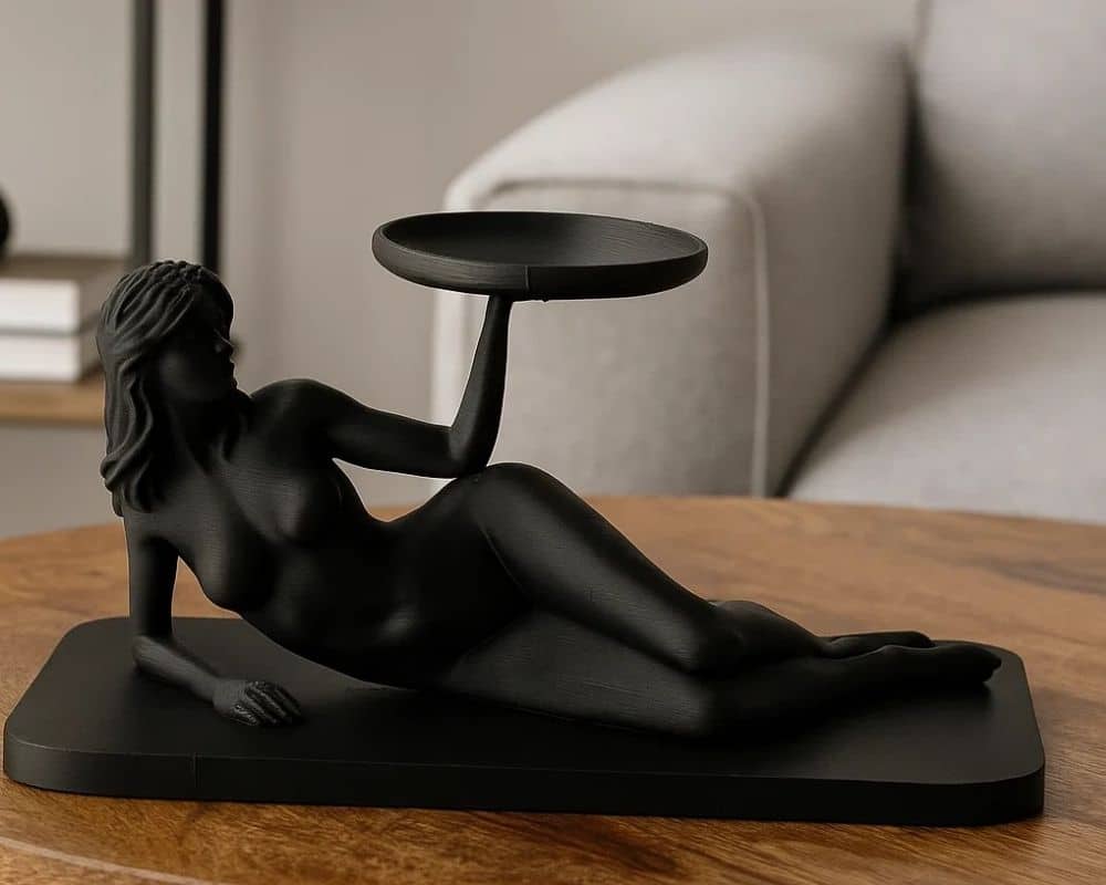 המגש תכשיטים בדמות אישה הוא פסל שחור של אישה שוכבת המחזיקה מגש קטן מעליה, מושלם לתצוגה על שולחן עץ בסלון מודרני.
