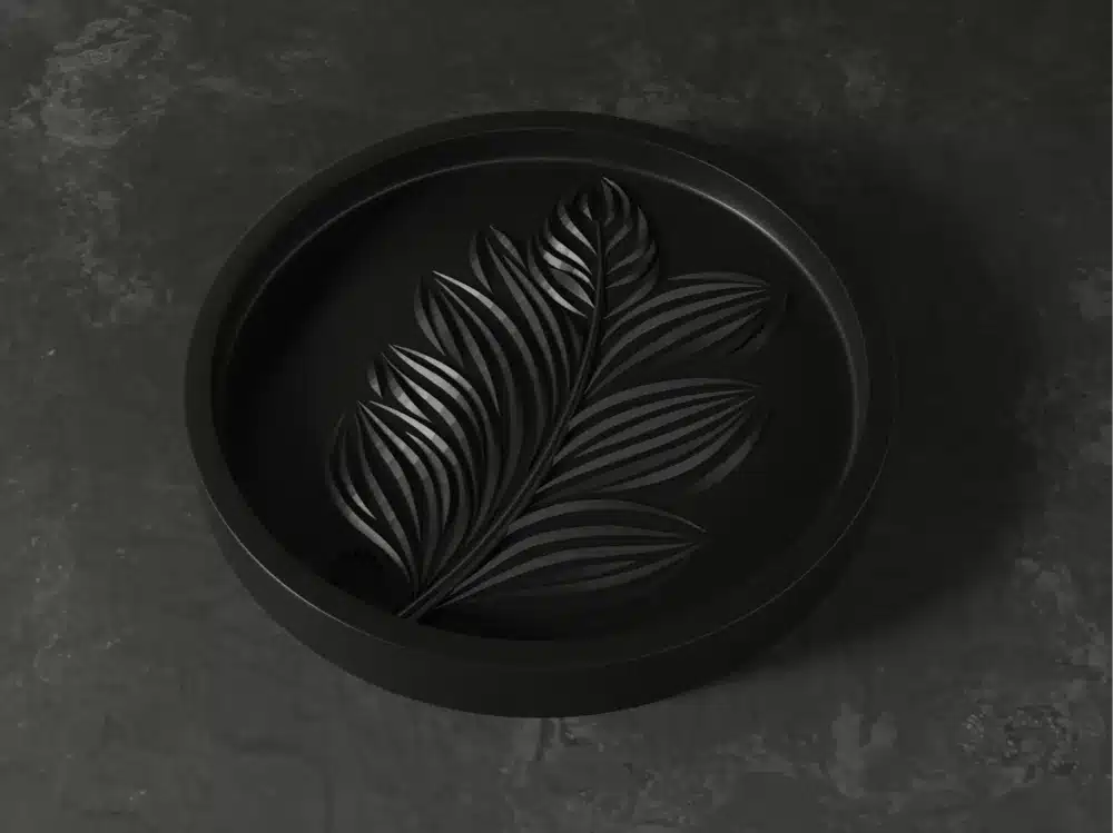 המגש מעוצב הוא מגש עגול בצבע שחור מט עם דפוס עלים מובלט של קווים חופפים על רקע כהה ומרקם.