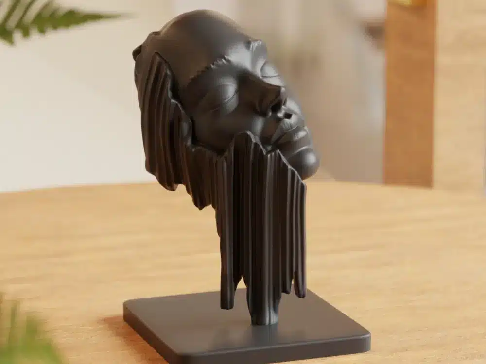 2025-04-16_a3190bf5237f9 פסל שחור מודרני של פנים אנושיות עם תווי פנים מוארכים, כאילו נמסו, על בסיס מרובע, מונח על משטח עץ. הרקע מטושטש קלות, עם רמזים לצמחים ורהיטים.